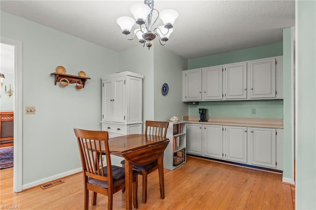 dining area featuring light wood finished floors, baseboards, visible vents, a textured ceiling, and a notable chandelier