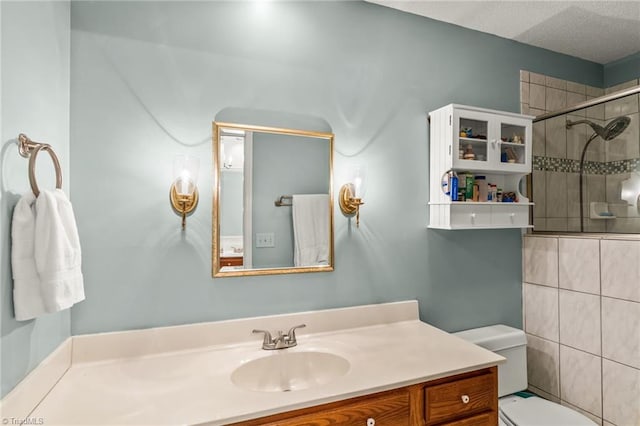 full bathroom with tiled shower, vanity, toilet, and a textured ceiling