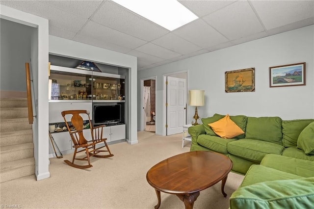 living area featuring carpet floors, stairway, and a drop ceiling