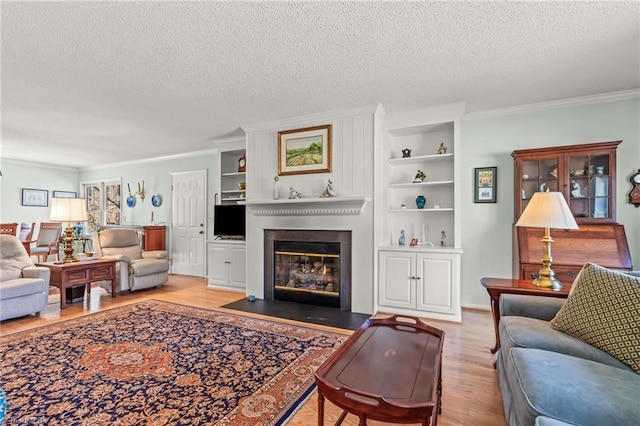 living room with a large fireplace, wood finished floors, a textured ceiling, crown molding, and built in shelves