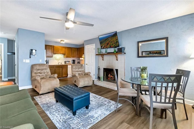 living room featuring a tiled fireplace, ceiling fan, and dark hardwood / wood-style floors