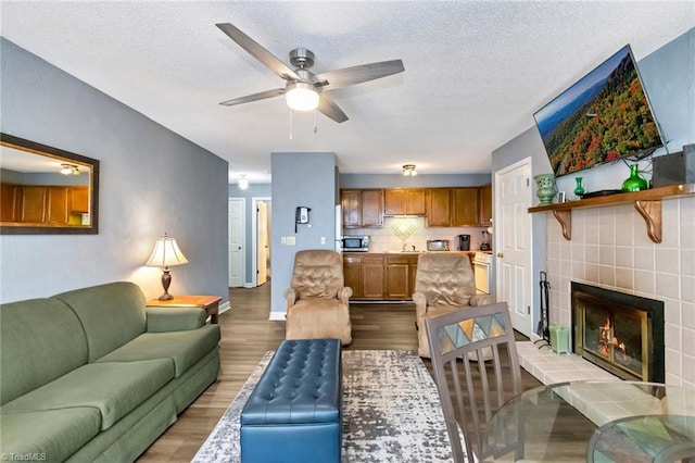 living room with a textured ceiling, light hardwood / wood-style flooring, ceiling fan, and a tiled fireplace