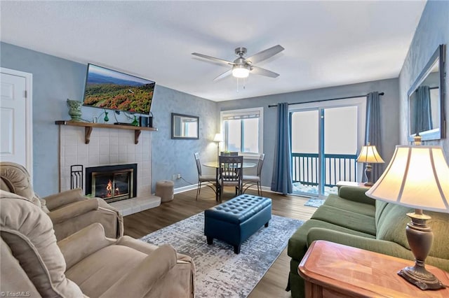 living room with a tile fireplace, wood-type flooring, and ceiling fan