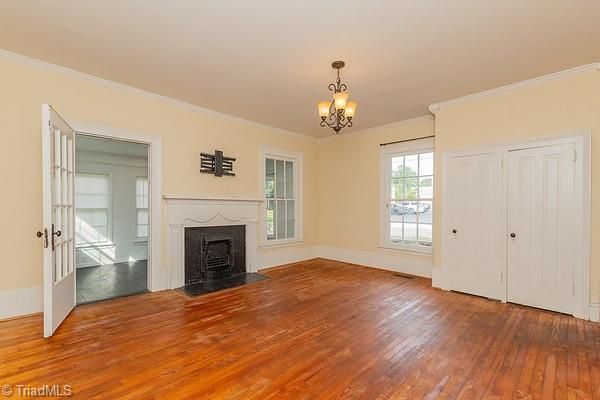 112 S Caldwell St, Salisbury, NC 28144 - unfurnished living room with wood-type flooring, a chandelier, a fireplace with flush hearth, and crown molding