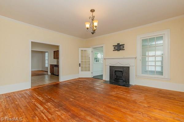 112 S Caldwell St, Salisbury, NC 28144 - unfurnished living room with crown molding, a chandelier, a fireplace with flush hearth, wood finished floors, and baseboards