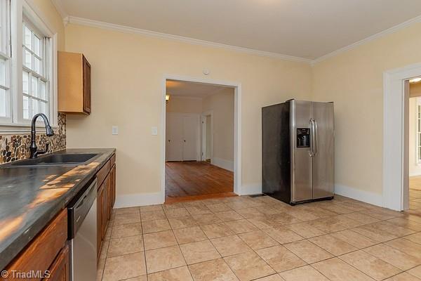 112 S Caldwell St, Salisbury, NC 28144 - kitchen with appliances with stainless steel finishes, a sink, crown molding, light tile patterned floors, and brown cabinetry