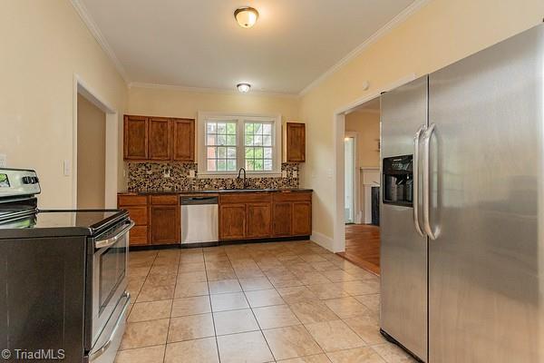 112 S Caldwell St, Salisbury, NC 28144 - kitchen featuring stainless steel appliances, dark countertops, crown molding, backsplash, and brown cabinetry