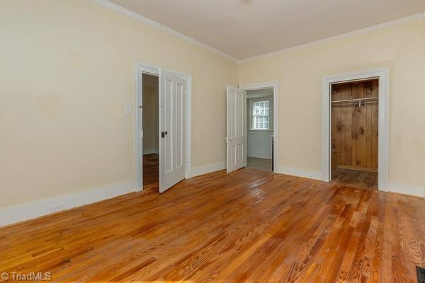 112 S Caldwell St, Salisbury, NC 28144 - unfurnished bedroom with ornamental molding, light wood-style floors, baseboards, a closet, and a walk in closet