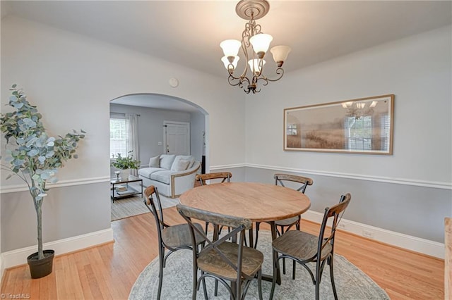 dining room with arched walkways, an inviting chandelier, wood finished floors, and baseboards
