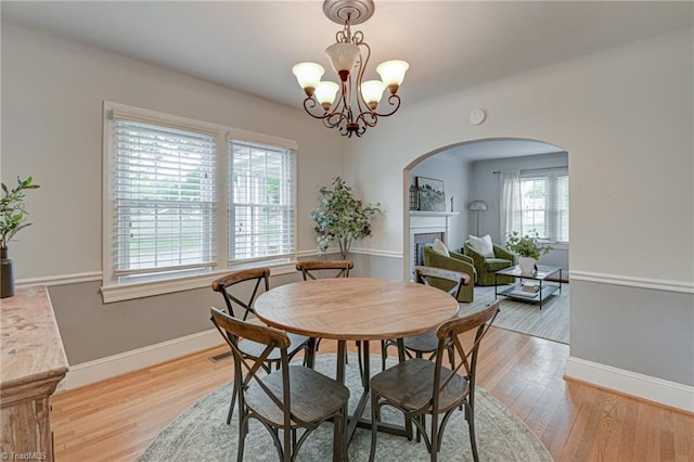 dining space with arched walkways, light wood-style floors, a fireplace, and a chandelier