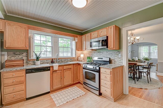 kitchen with stainless steel appliances, a sink, light wood-style floors, and tasteful backsplash
