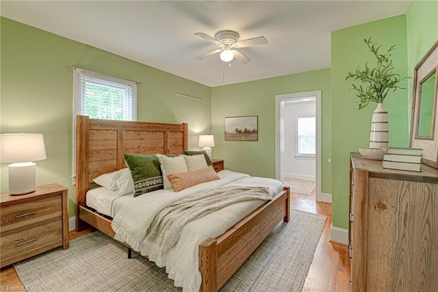 bedroom featuring ceiling fan, baseboards, multiple windows, and light wood-type flooring