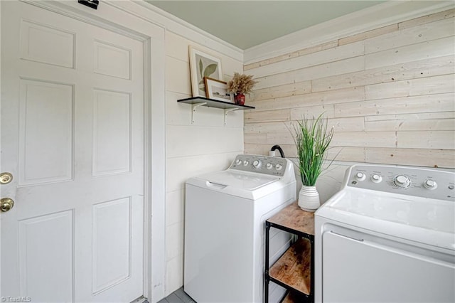 clothes washing area with washer and clothes dryer, wood walls, ornamental molding, and laundry area
