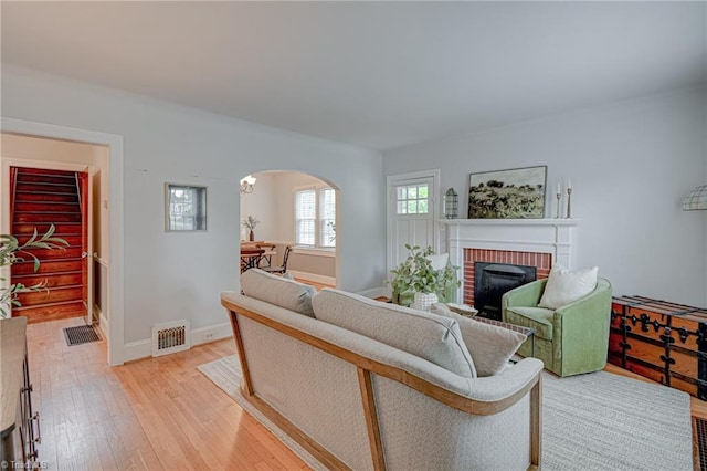 living area with light wood-style flooring, arched walkways, baseboards, visible vents, and a brick fireplace
