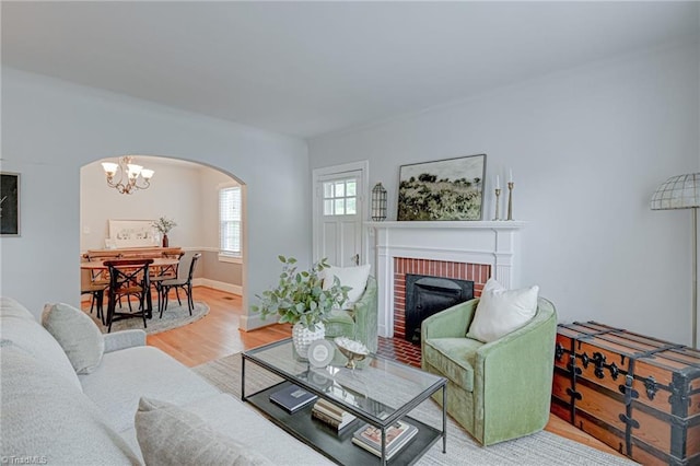 living area with arched walkways, a notable chandelier, wood finished floors, and a fireplace