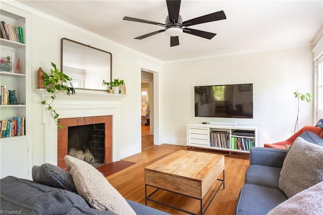living area featuring hardwood / wood-style flooring, ornamental molding, ceiling fan, a tile fireplace, and baseboards