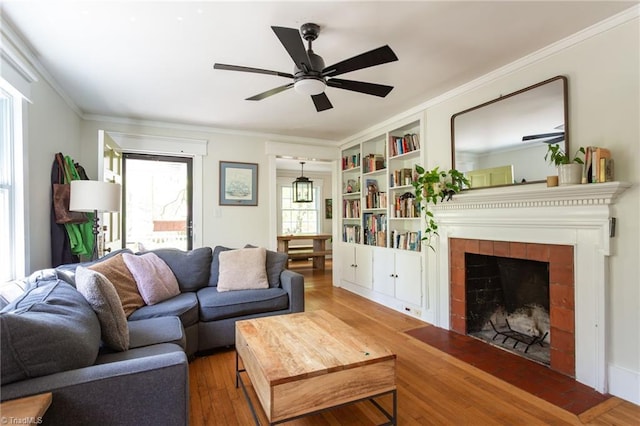 living area with a tile fireplace, a ceiling fan, wood finished floors, ornamental molding, and built in features