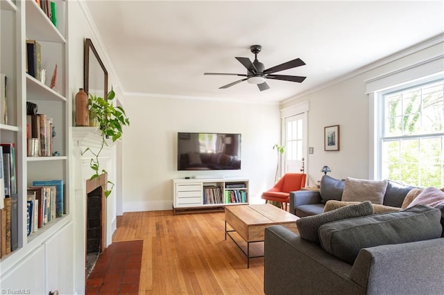 living area featuring plenty of natural light, wood-type flooring, ceiling fan, a fireplace with flush hearth, and crown molding