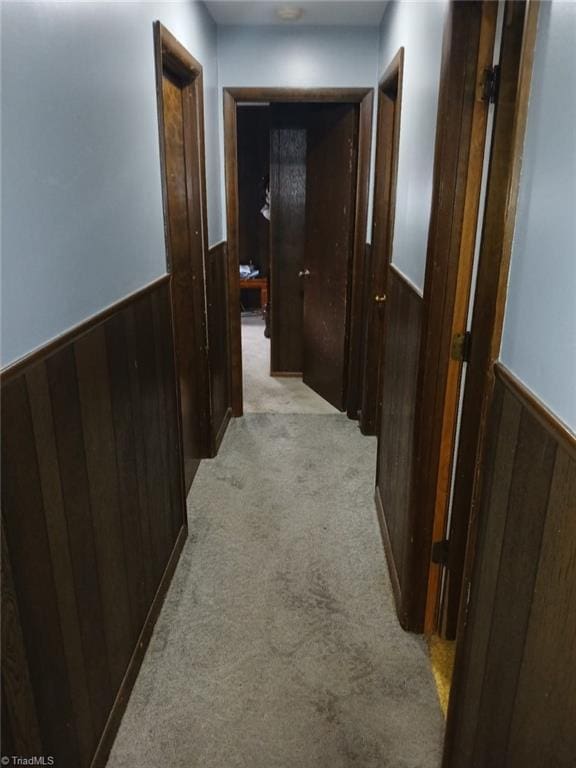 hall featuring light carpet and wooden walls