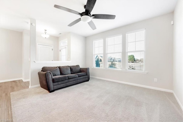 living area with light carpet, ceiling fan, and baseboards