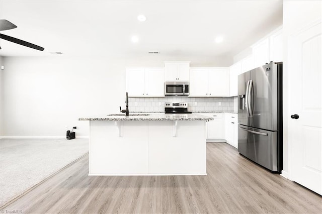 kitchen with light stone counters, a sink, white cabinetry, appliances with stainless steel finishes, and an island with sink