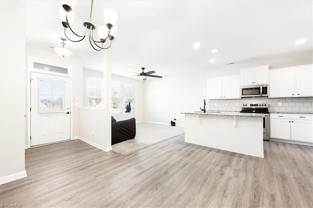 kitchen featuring stainless steel appliances, open floor plan, white cabinets, and an island with sink