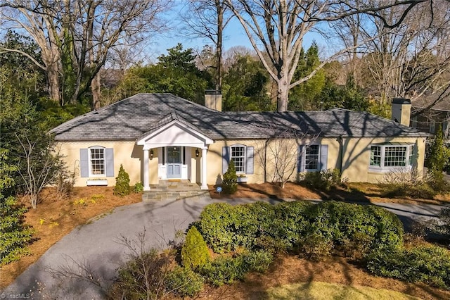 ranch-style house featuring aphalt driveway, a chimney, and stucco siding