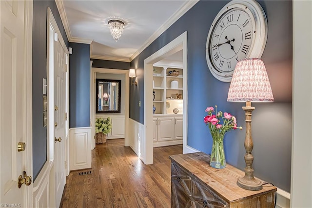 entryway featuring built in features, visible vents, wainscoting, wood finished floors, and crown molding