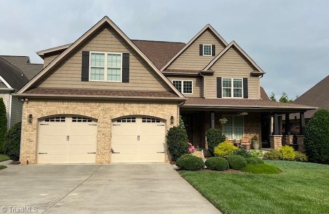2507 Duck Club Rd, Greensboro, NC 27410 - craftsman-style house with driveway, a front lawn, brick siding, covered porch, and a garage