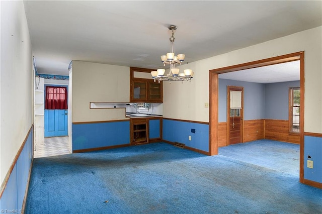 kitchen featuring dark colored carpet, decorative light fixtures, wood walls, and a chandelier