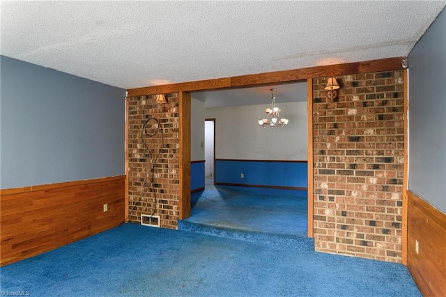 unfurnished room with wood walls, a notable chandelier, dark carpet, and a textured ceiling