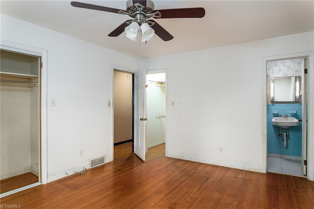 unfurnished bedroom with ceiling fan, tile walls, hardwood / wood-style floors, connected bathroom, and a closet