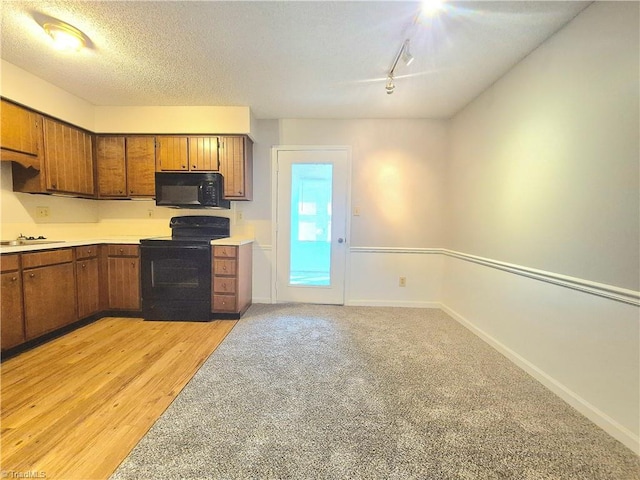 1018 Cedar Place Ct, Winston-Salem, NC 27107 - kitchen with black appliances, brown cabinetry, rail lighting, light countertops, and light wood-style flooring