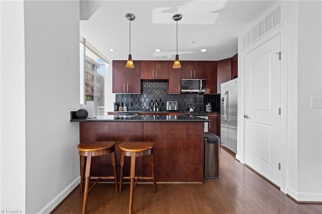 kitchen featuring dark hardwood / wood-style flooring, appliances with stainless steel finishes, hanging light fixtures, kitchen peninsula, and decorative backsplash