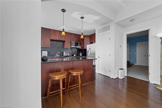 kitchen featuring backsplash, appliances with stainless steel finishes, dark hardwood / wood-style flooring, kitchen peninsula, and a breakfast bar