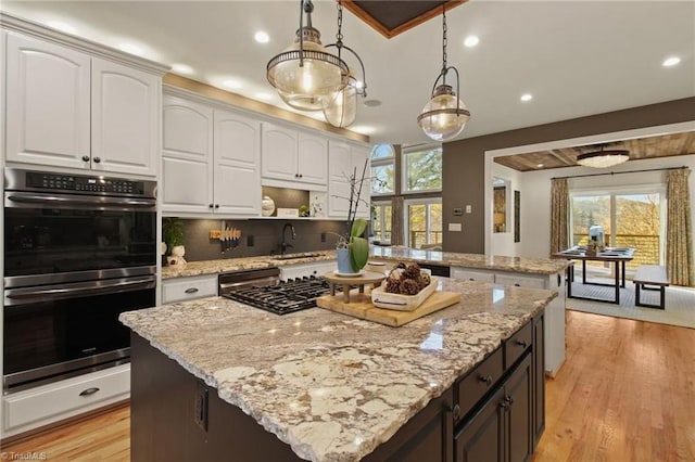 kitchen with hanging light fixtures, a kitchen island, stainless steel appliances, and white cabinetry