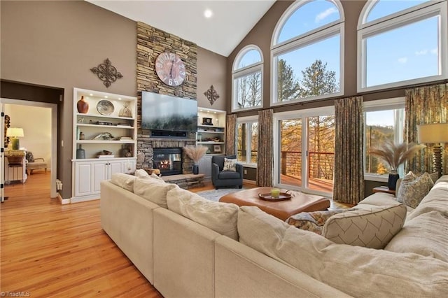 living room with high vaulted ceiling, built in shelves, light hardwood / wood-style flooring, and a fireplace