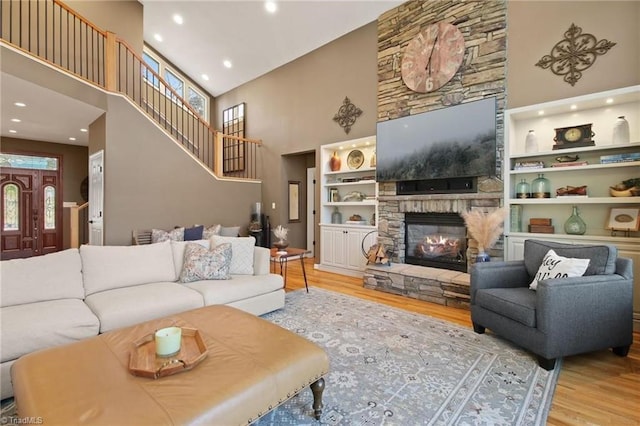 living room with a high ceiling, built in shelves, a stone fireplace, and light wood-type flooring