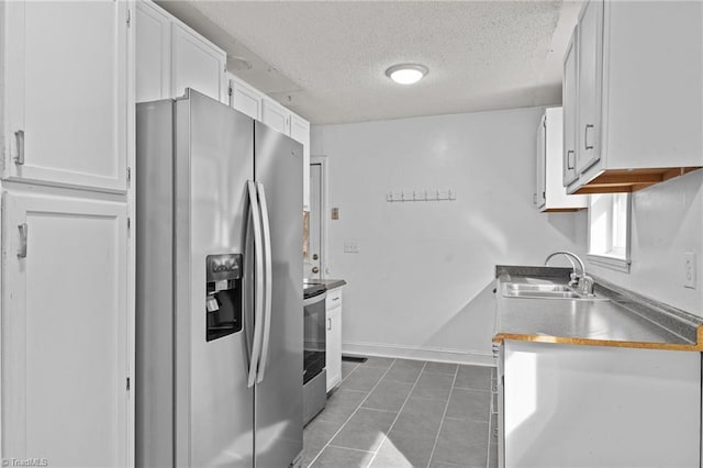 kitchen with sink, a textured ceiling, dark tile patterned floors, stainless steel appliances, and white cabinets