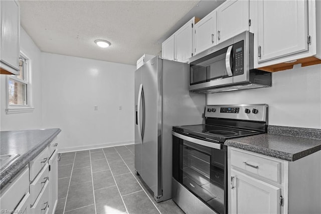 kitchen with stainless steel appliances, dark tile patterned floors, white cabinets, and a textured ceiling