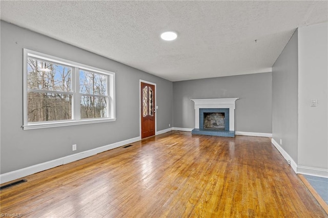 unfurnished living room with a brick fireplace, wood-type flooring, and a textured ceiling