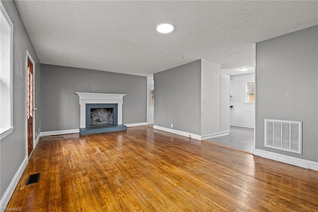 unfurnished living room featuring wood-type flooring, a brick fireplace, and a textured ceiling