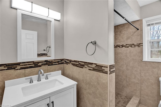 bathroom with tile walls, wainscoting, a tile shower, and vanity