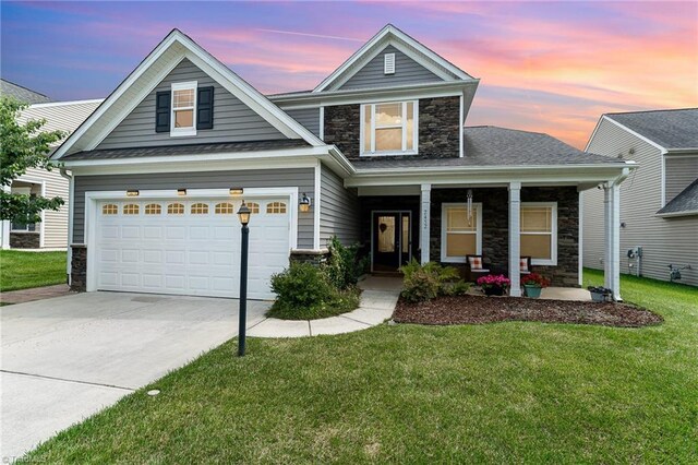 2452 Tannin Ct, High Point, NC 27265 - view of front of home with stone siding, covered porch, a yard, concrete driveway, and a shingled roof