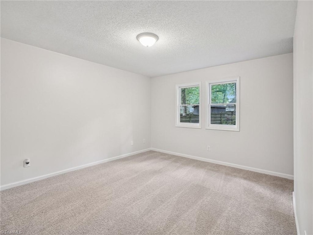 carpeted spare room featuring a textured ceiling and baseboards