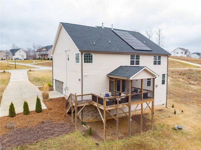 back of property with a garage, a sunroom, a wooden deck, and solar panels