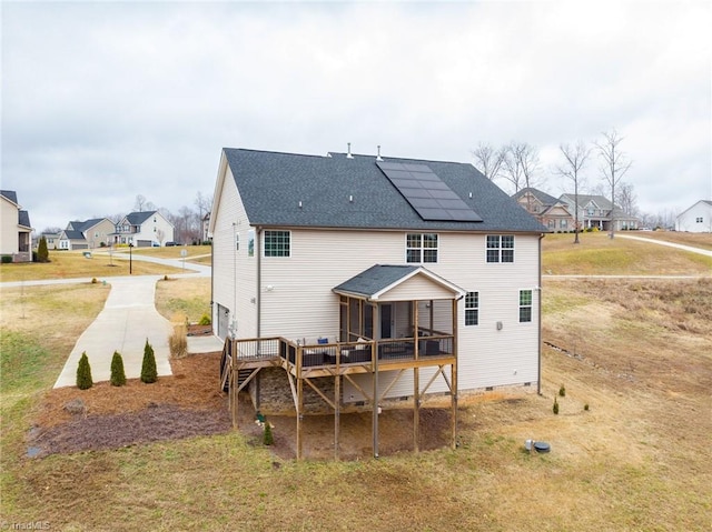 rear view of house featuring a yard, a sunroom, a wooden deck, and solar panels