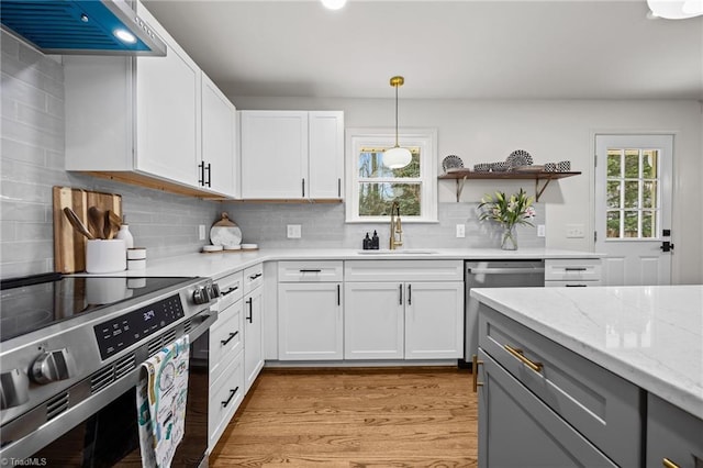 kitchen with light wood-style flooring, a sink, light stone counters, stainless steel appliances, and wall chimney range hood