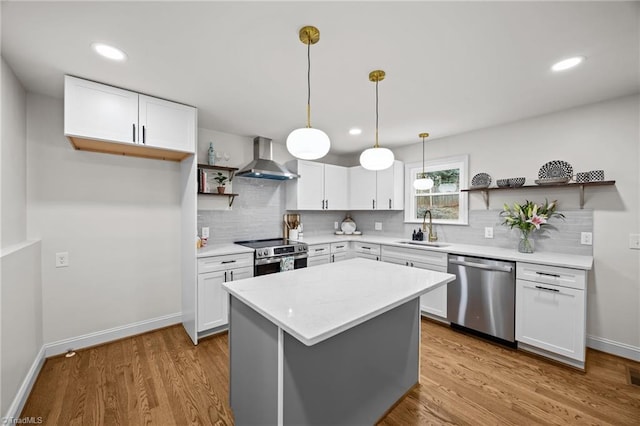 kitchen featuring open shelves, wall chimney range hood, appliances with stainless steel finishes, wood finished floors, and a sink