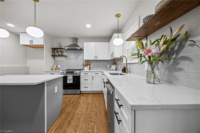 kitchen with light wood-style flooring, open shelves, a sink, stainless steel appliances, and wall chimney range hood